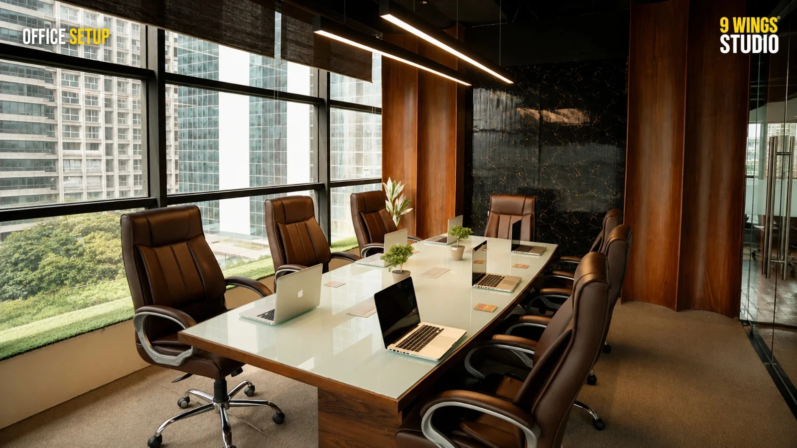 Modern office conference room with a large glass table, leather chairs, laptops, wood-paneled walls, and floor-to-ceiling city views.